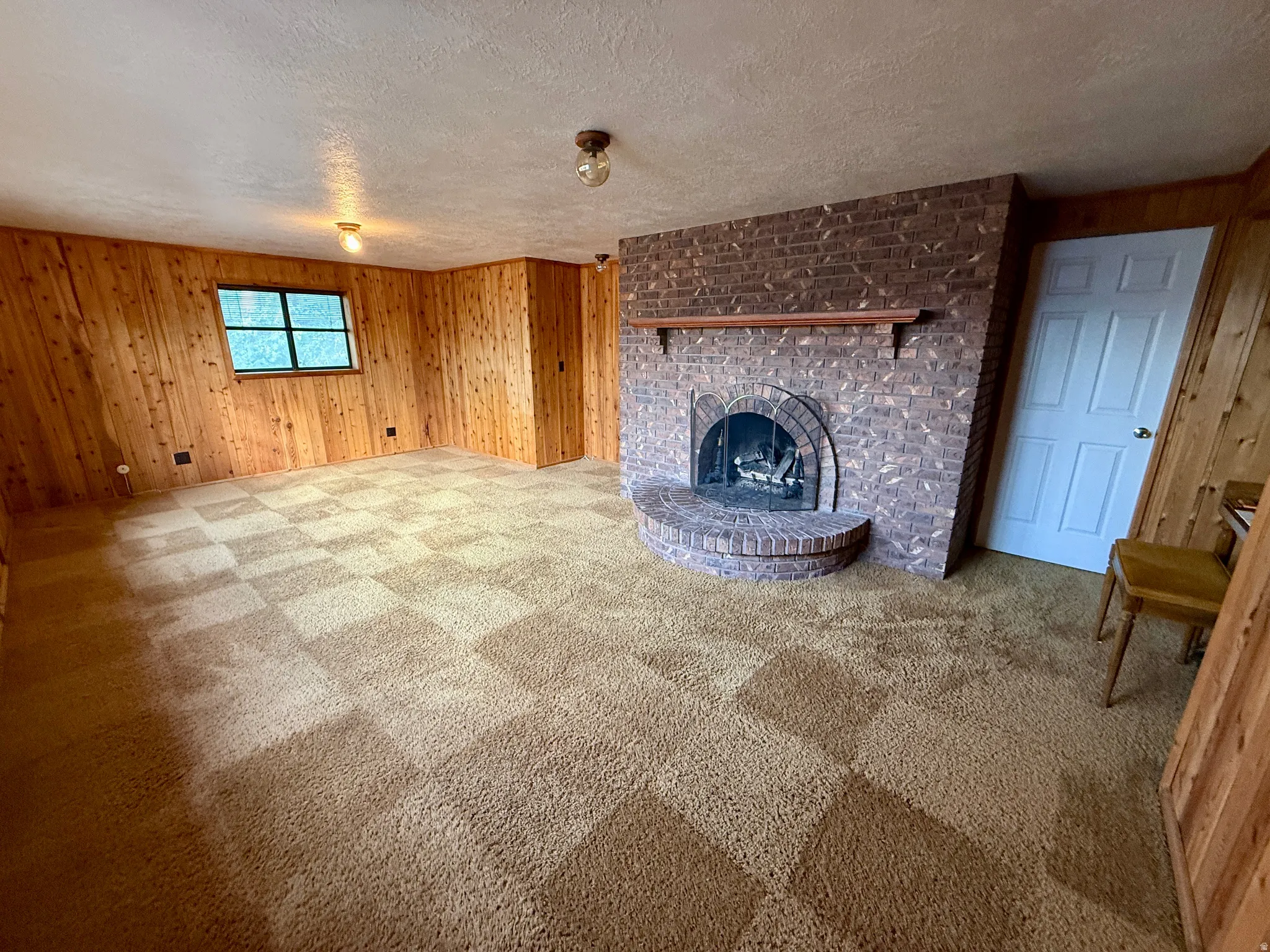 Brick fireplace with a hearth, wood mantle, wood paneling, and wall-to-wall carpeting