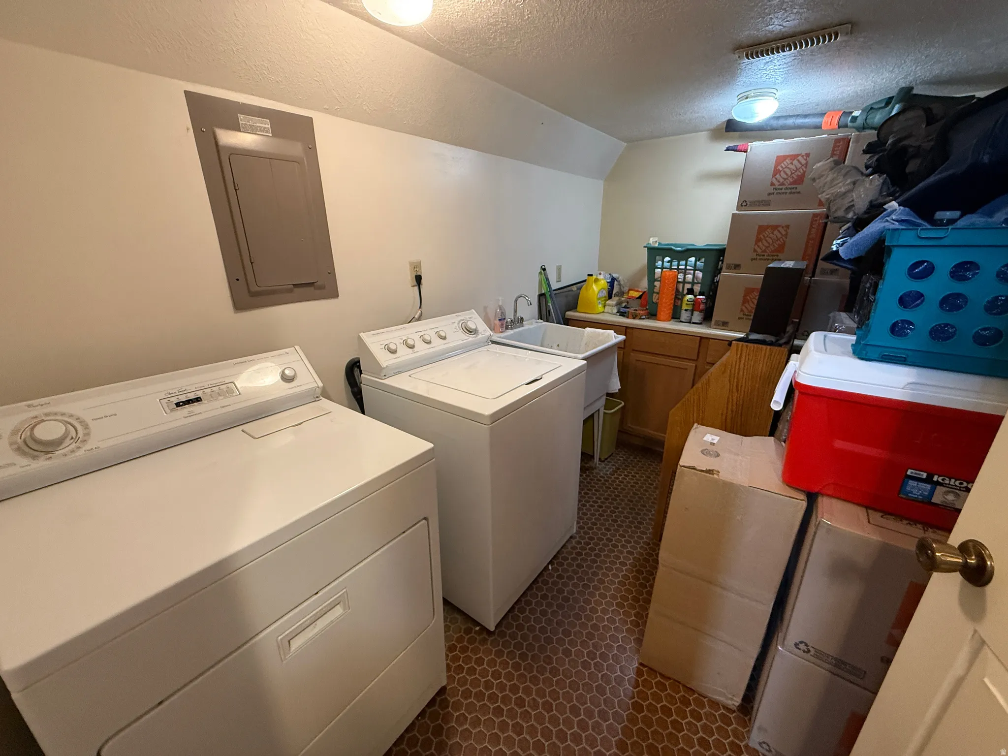 Dedicated laundry room featuring side-by-side washer and dryer appliances, ample counter space for folding and sorting, wood-finish cabinetry for storage, and tile flooring throughout