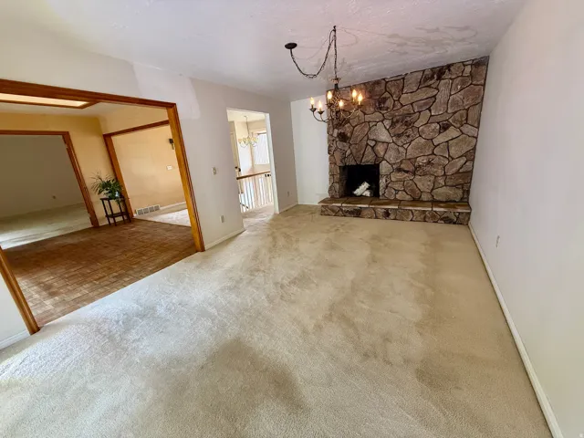 Spacious living area featuring a stone fireplace with hearth, an ornate chandelier, and carpet flooring