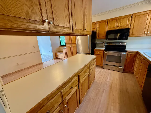 Kitchen featuring wood cabinetry, light countertops, and stainless steel appliances including a range, microwave, and refrigerator