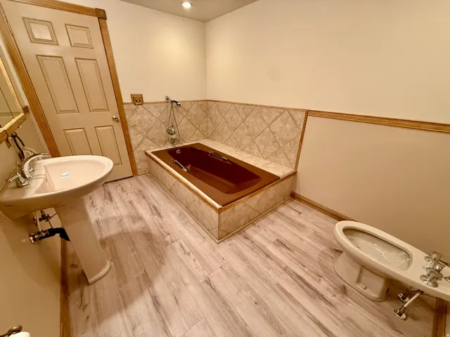 Pedestal sink with chrome fixtures, built-in bathtub with tiled surround, Bidet, light wood-finish flooring, and recessed ceiling lighting