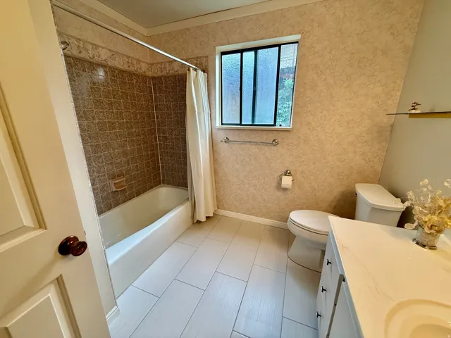 Bathroom 2 on main level- White tile flooring, a built-in bathtub with tiled surround, a white toilet, and a white vanity with an integrated sink