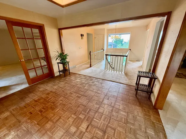 Parquet wood-finish flooring, wood-framed French doors, open staircase with wood handrails, and a transom window