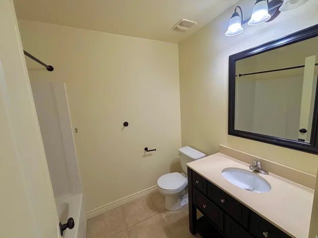 Bathroom featuring a dark wood-finish vanity with a light countertop, a framed mirror, an overhead vanity light, and tiled flooring