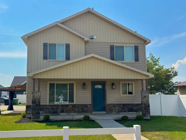 Two-story residence featuring light siding and darker stone veneer accents, an inviting covered front porch, a vibrant blue entry door, and dark decorative window shutters