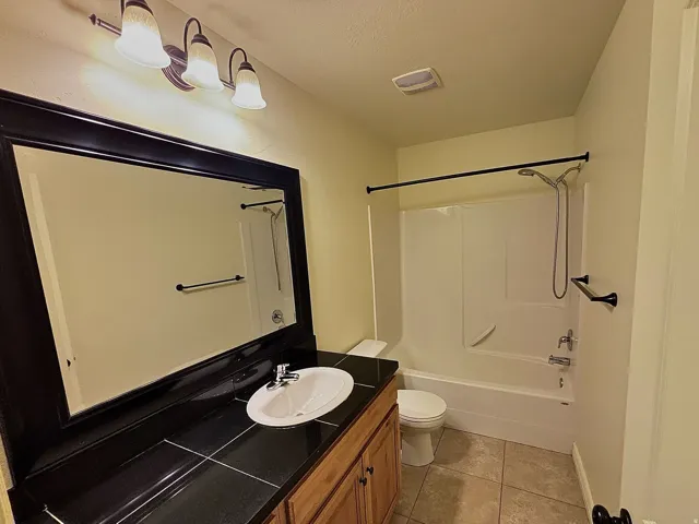 Vanity with wood-finish cabinetry, a tile countertop, and an oval undermount sink