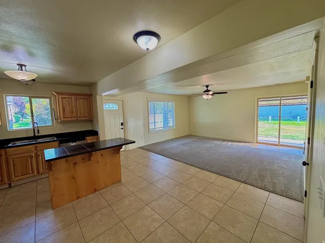 Kitchen with wood cabinetry and dark countertops, tile flooring, and an island with a breakfast bar
