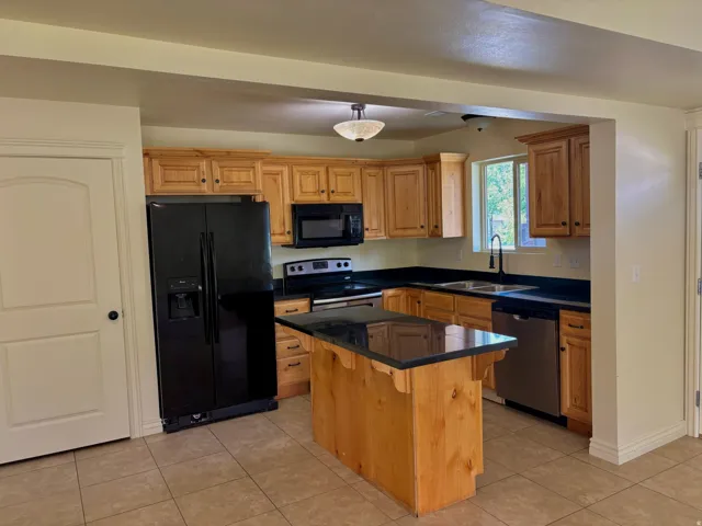Kitchen with wood cabinetry, black appliances, dark countertops, and a central island