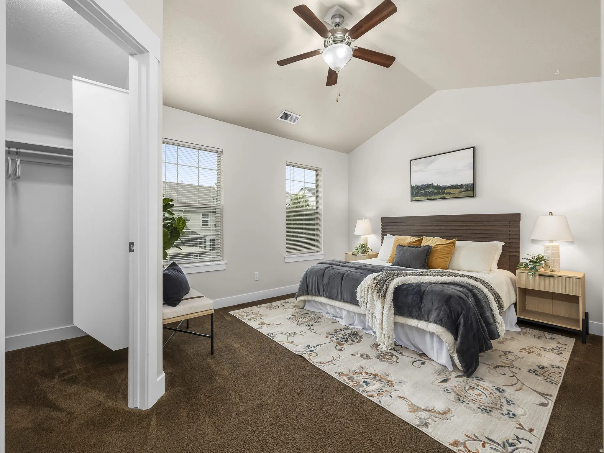 Vaulted ceiling with a ceiling fan, two windows, carpet flooring, and an open closet