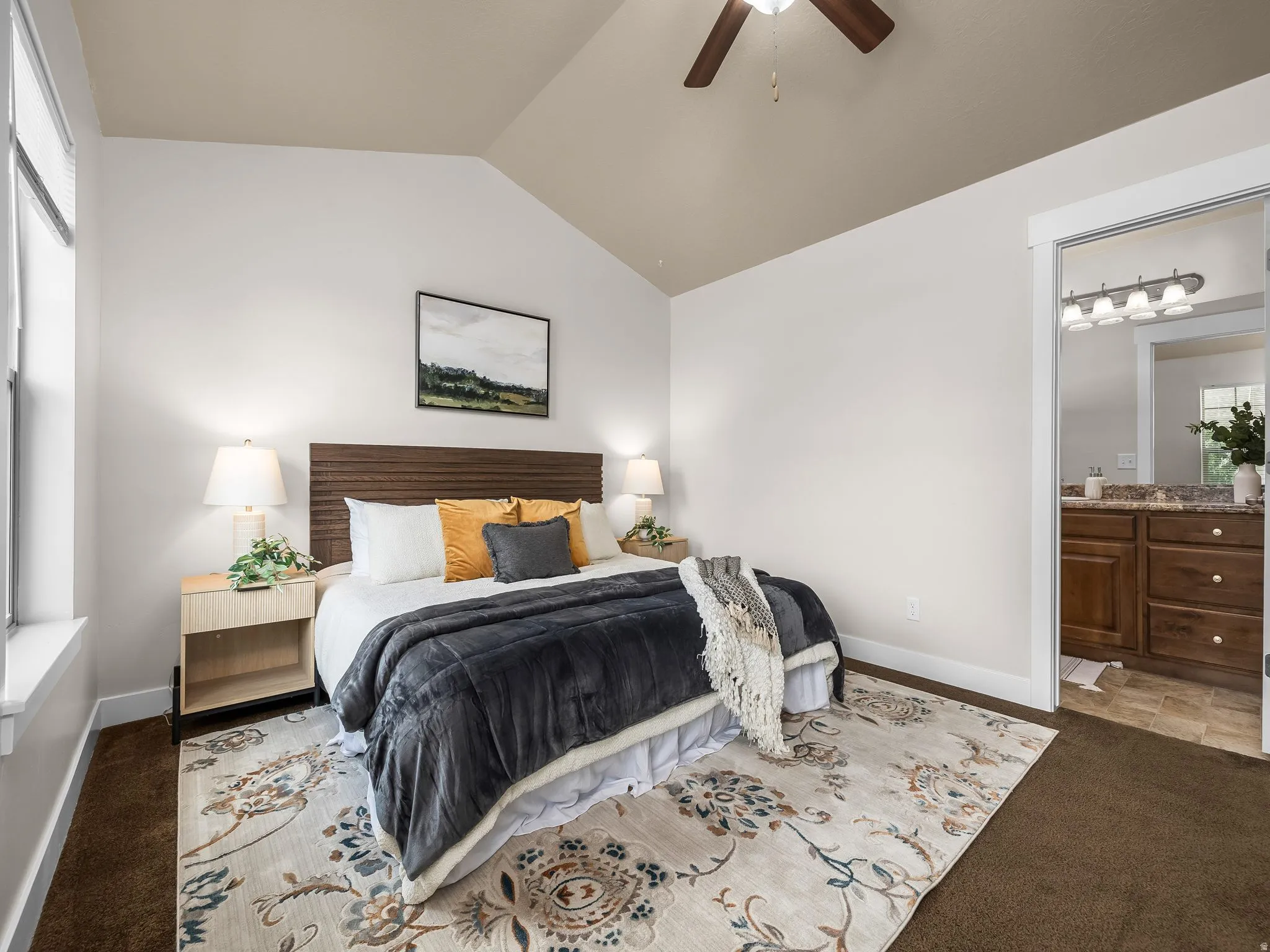 Vaulted ceiling, ceiling fan, wood-finish headboard, window, and wood-finish vanity with countertop