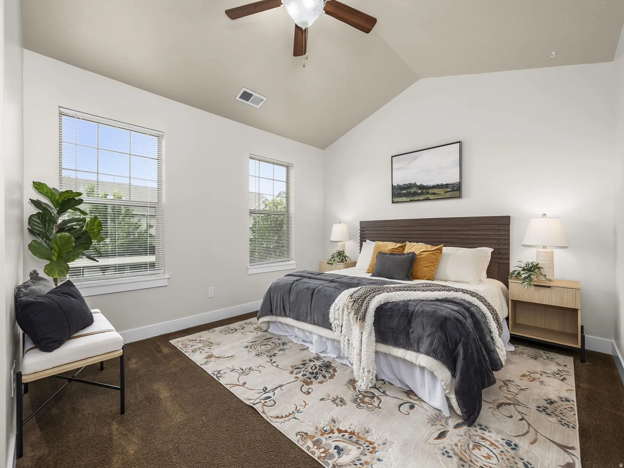 Vaulted ceiling with a ceiling fan, two windows with blinds, brown carpet flooring, and a wood-slat headboard