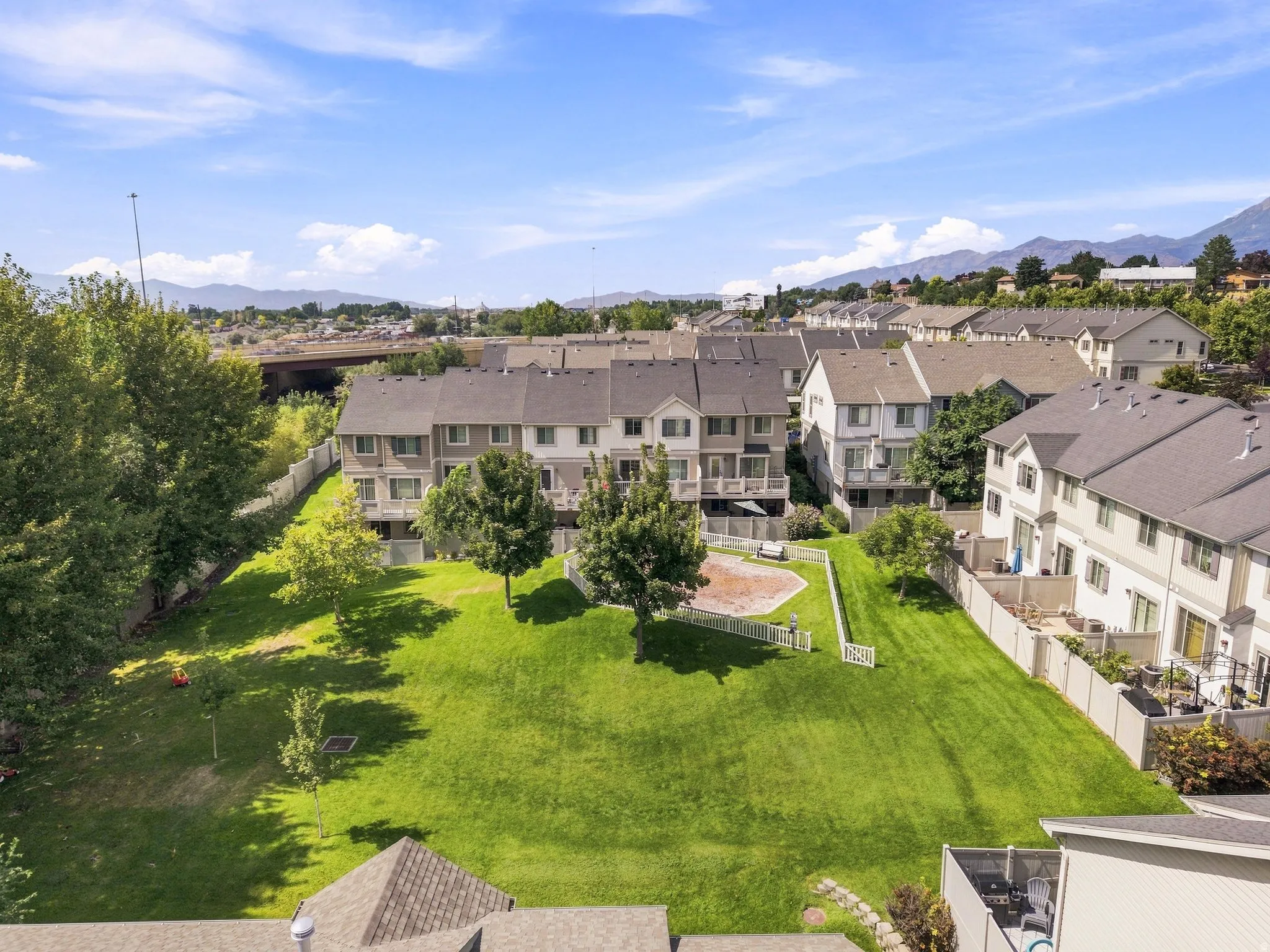 Expansive green space with mature trees, fenced perimeter, and a gravel play area
