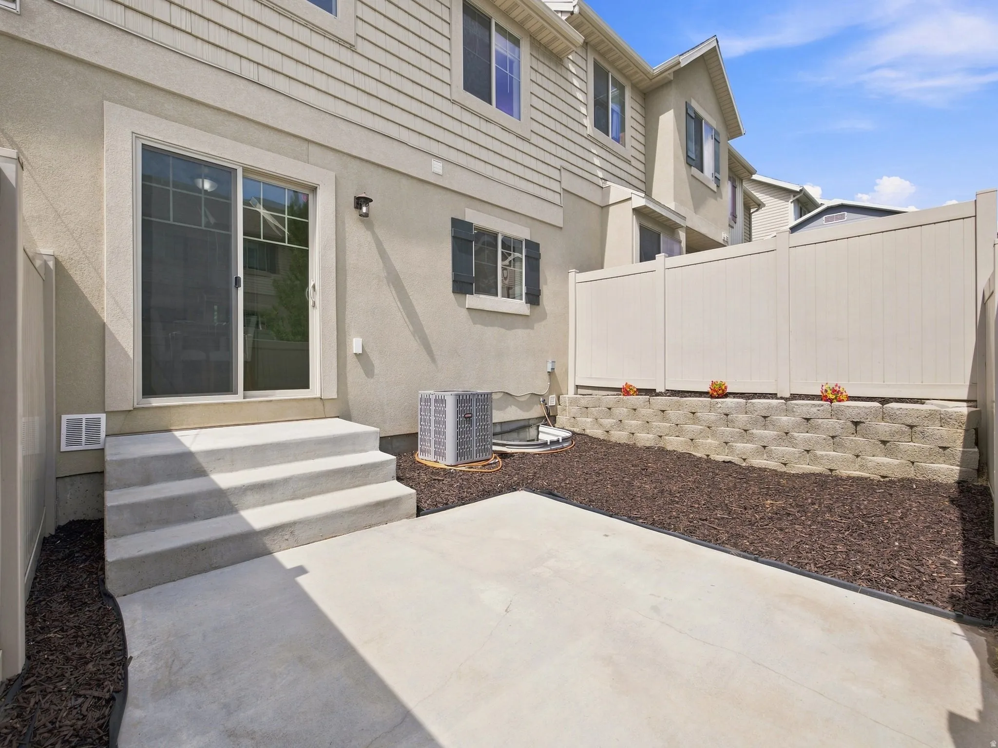 Concrete patio with a three-step entry, sliding glass door, and a retaining wall