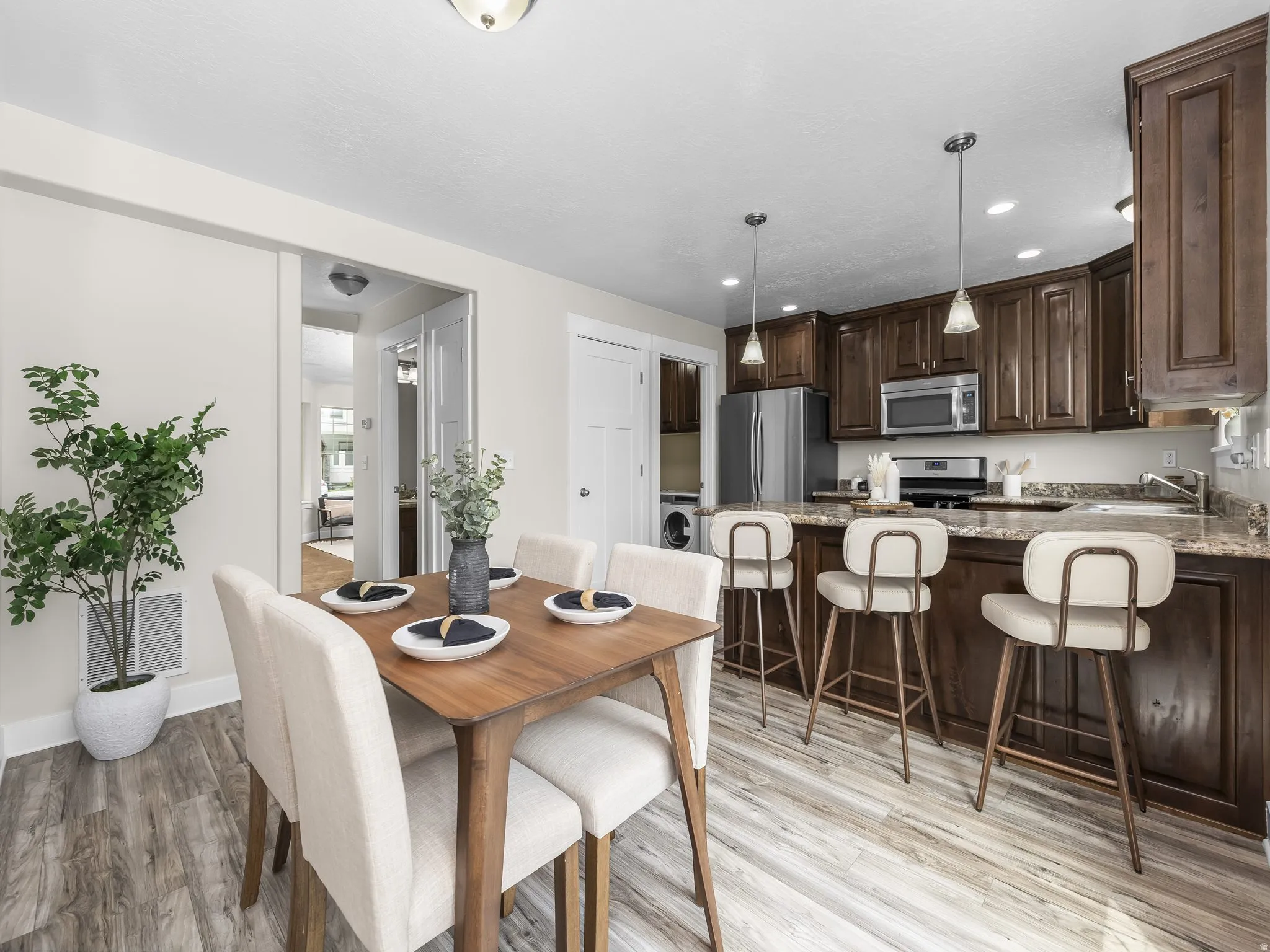 Kitchen featuring rich wood cabinetry, stainless steel appliances, a breakfast bar, pendant lighting, and wood-finish flooring