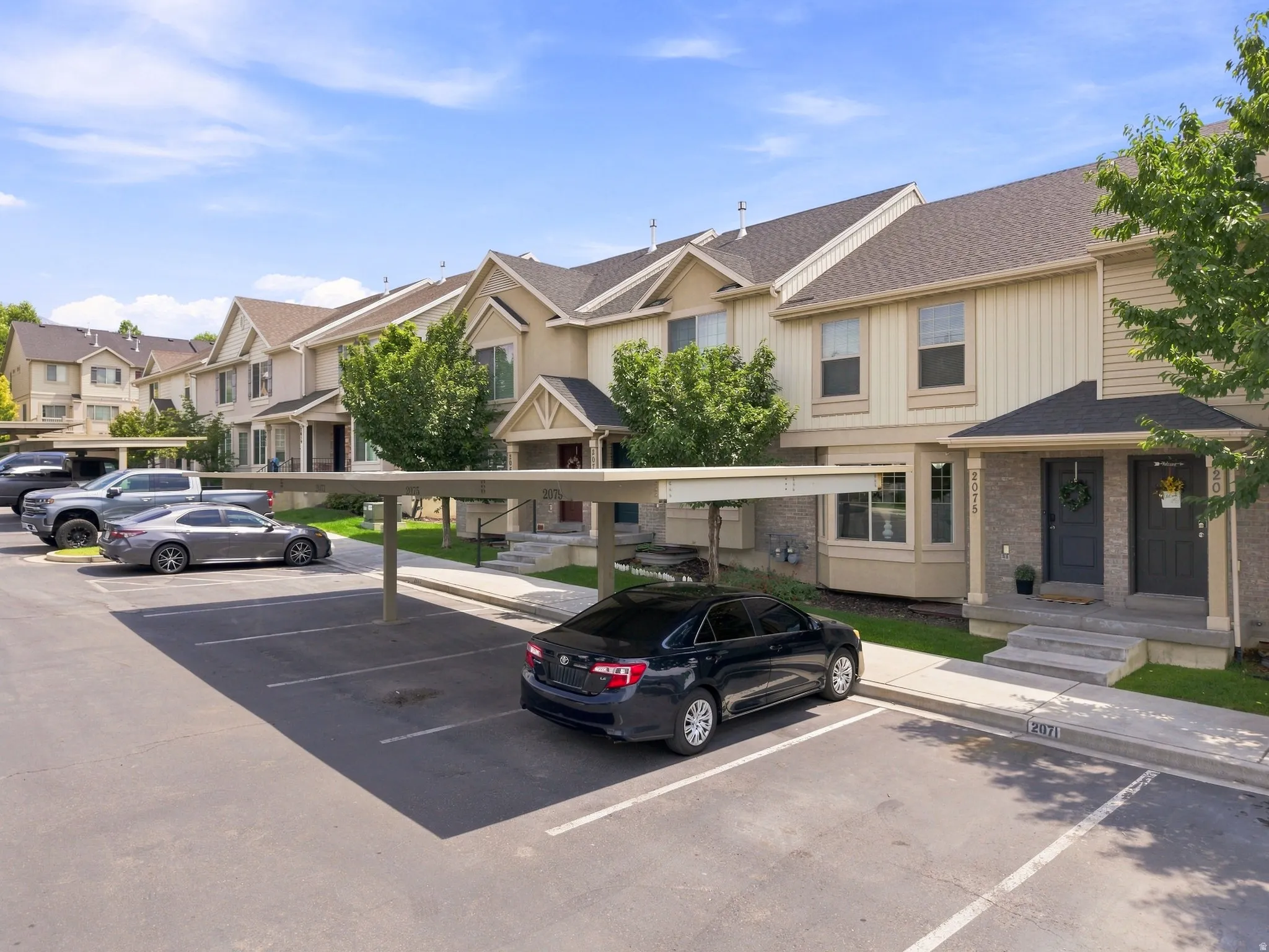 Multi-level townhome-style units featuring covered parking, dark shingle roofs, and light-toned siding