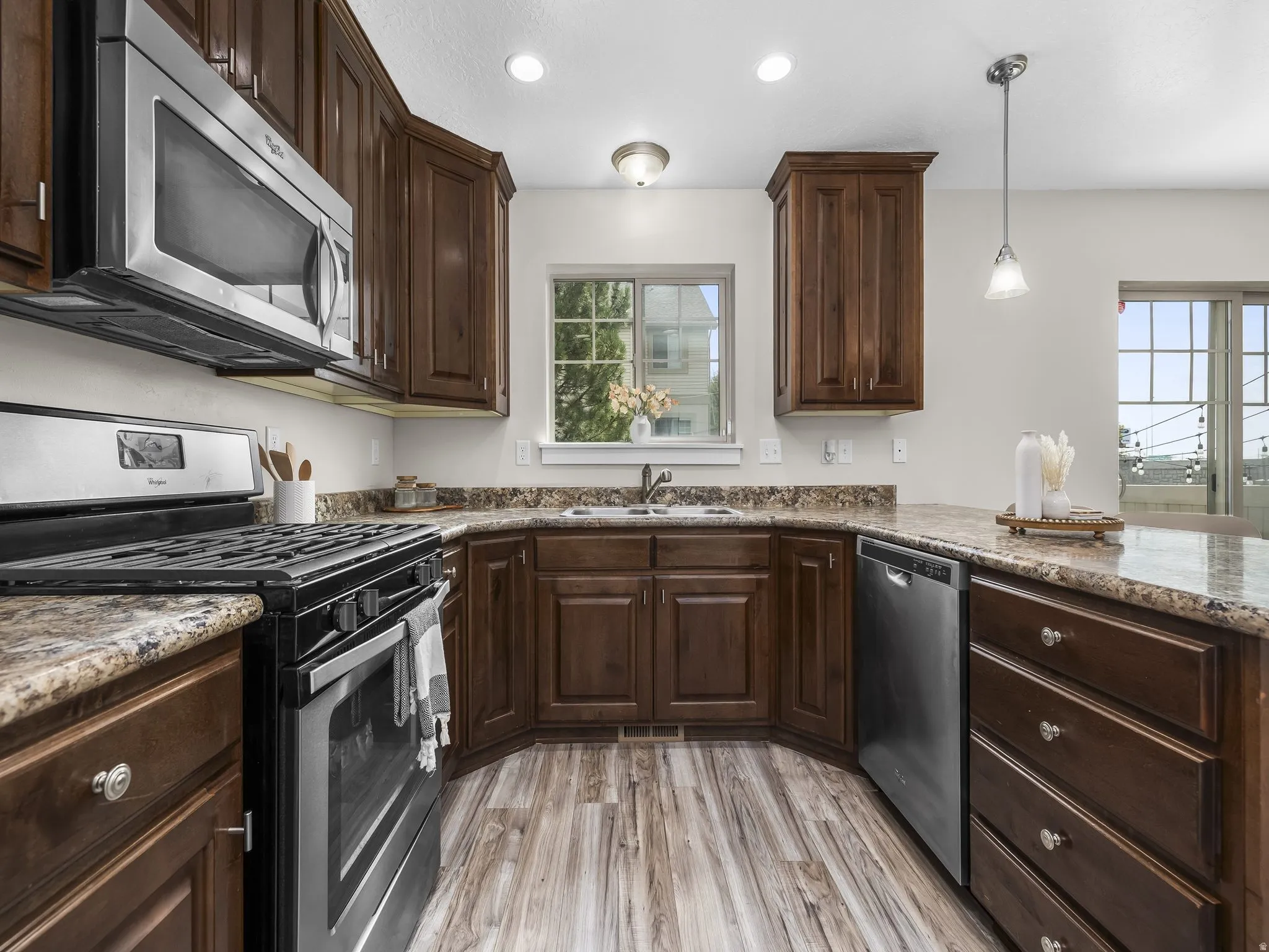 Kitchen featuring wood-finish flooring, dark wood cabinetry, stainless steel appliances, and a window