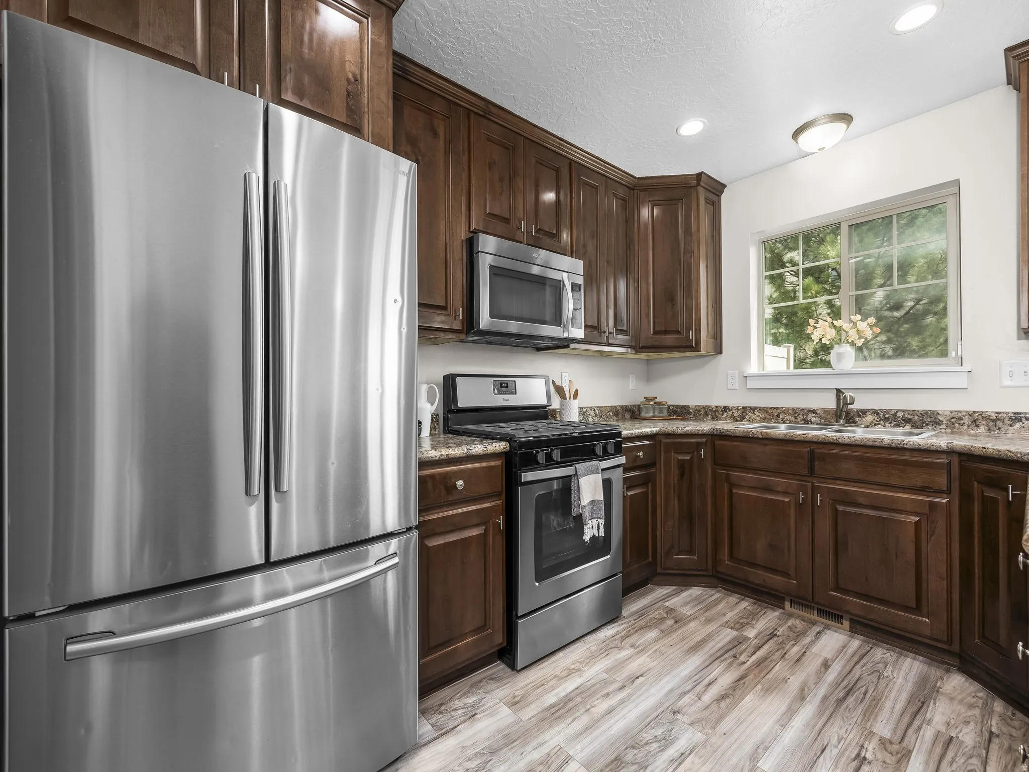 Kitchen featuring wood-finish flooring, dark wood cabinetry, stainless steel appliances, and a window above the sink