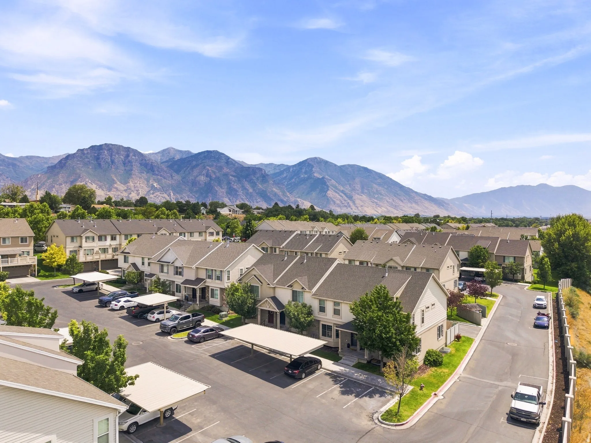 Community featuring a mountain backdrop, multiple residential buildings with gabled roofs, designated parking areas, and covered parking structures