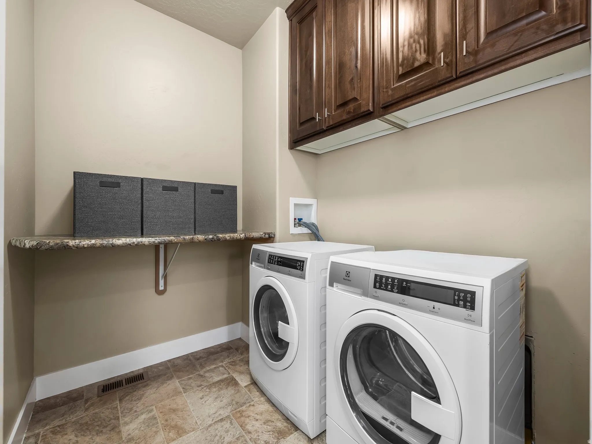Laundry area featuring wood-finish cabinetry, a patterned countertop, and tiled flooring