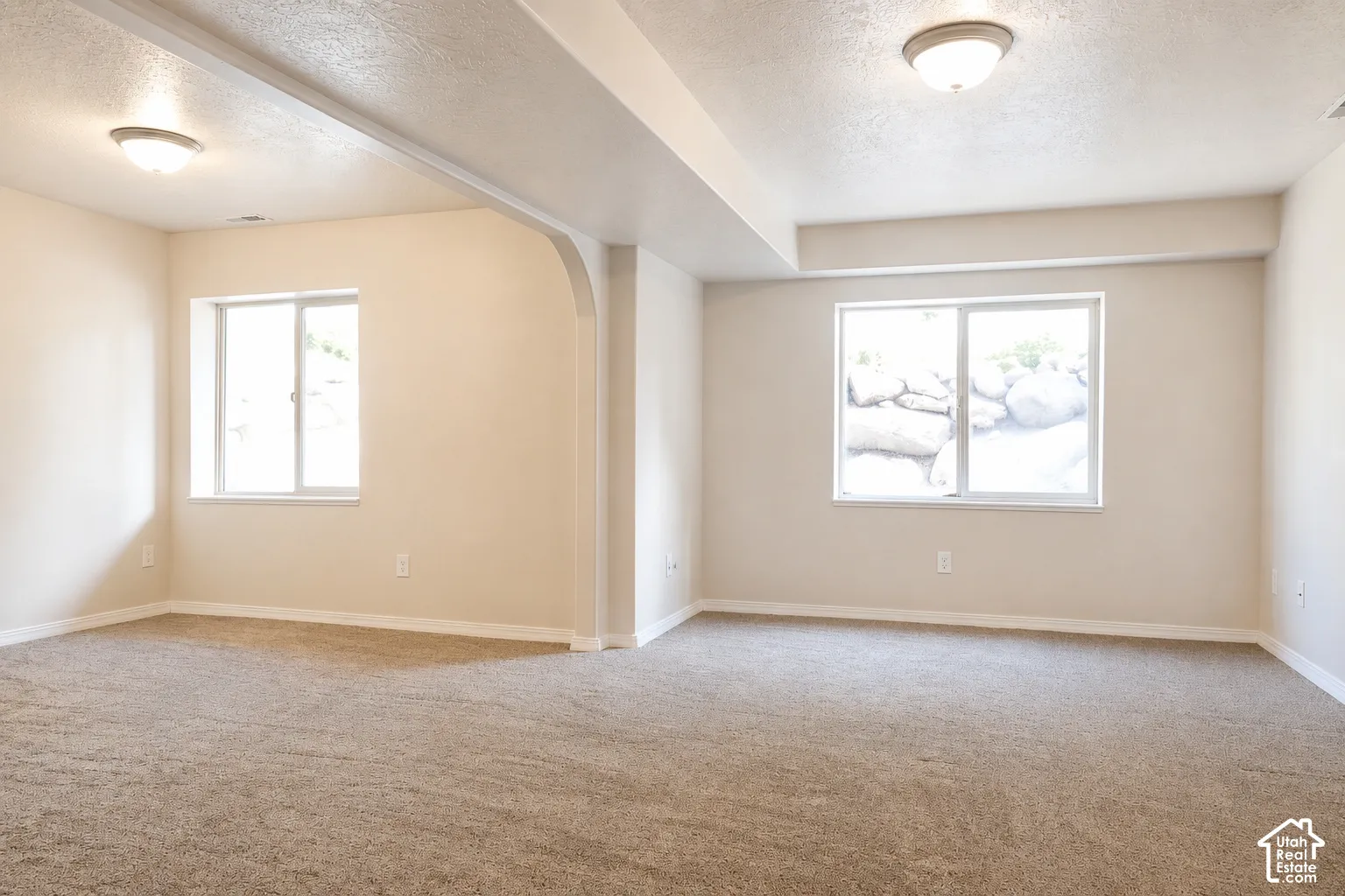 Expansive room featuring neutral-toned carpeting, two windows, recessed ceiling lights, and an architectural archway