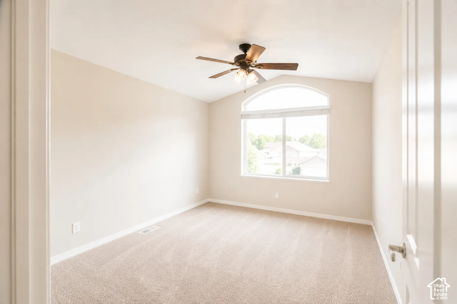 Vaulted ceilings with a ceiling fan, arched window, soft neutral wall color, and carpeted flooring