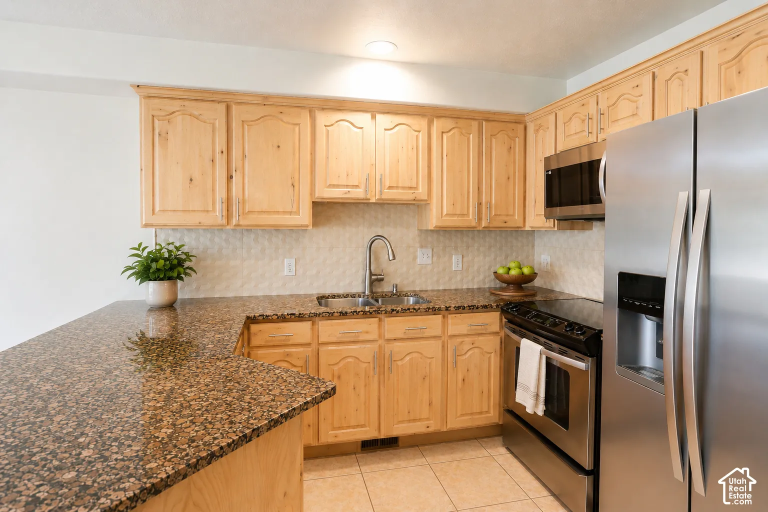 Kitchen with wood cabinetry, speckled countertops, stainless steel appliances, and a tile backsplash