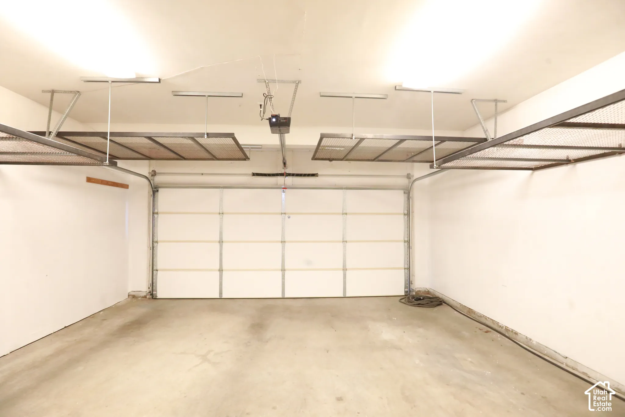 Concrete flooring garage with an automatic sectional garage door, overhead lighting, and two overhead storage racks