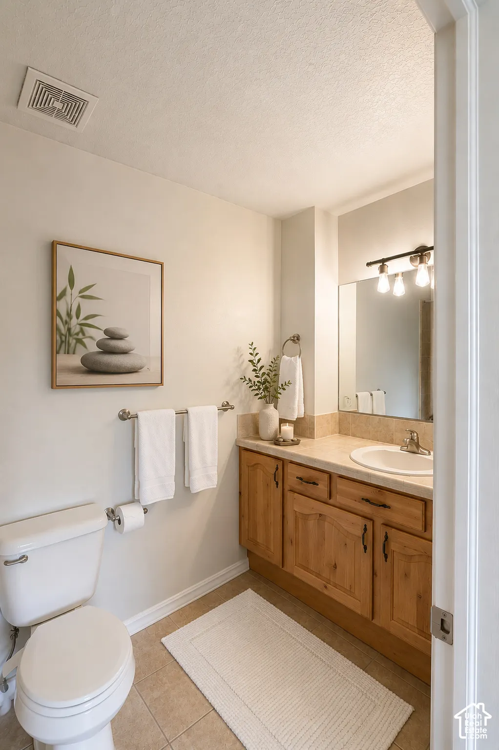 Spa-inspired bathroom featuring warm wood cabinetry with ample storage, ceramic tile flooring, and a framed mirror with integrated vanity lighting