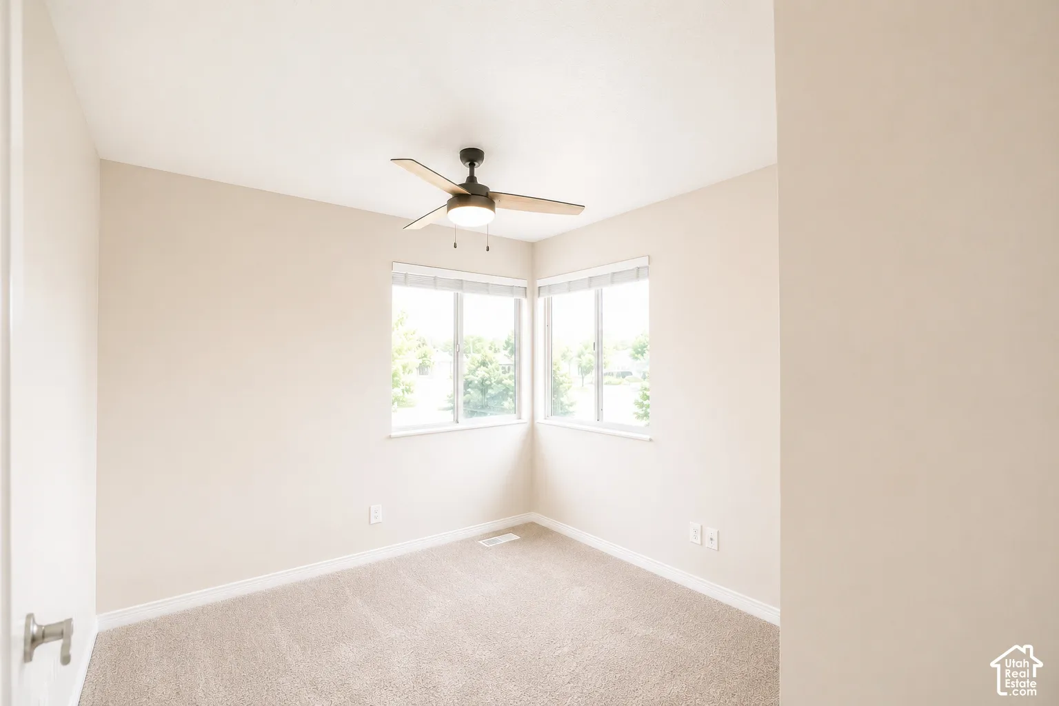 Neutral tone walls, carpeted flooring, corner windows with blinds, and ceiling fan with integrated lighting