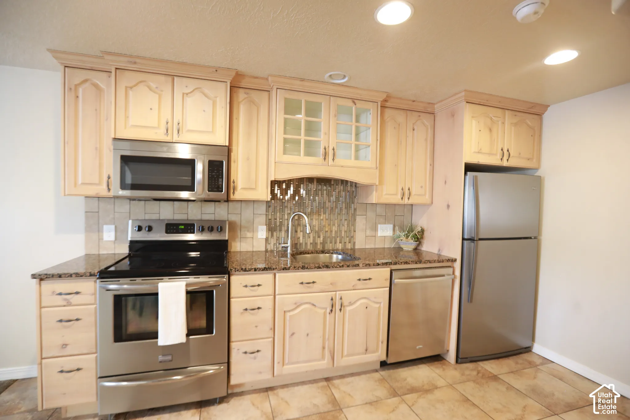 Kitchen featuring wood cabinetry, stainless steel appliances, granite-look countertops, tile backsplash, and recessed lighting