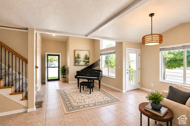 Vaulted ceilings with exposed beams, tile flooring, and an open staircase with decorative iron balusters