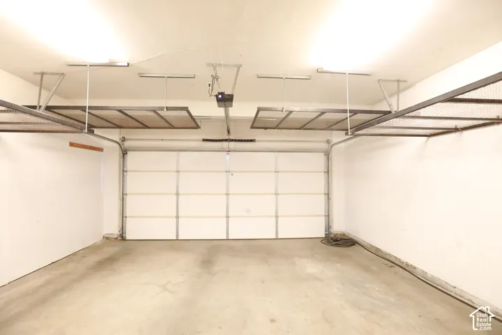 Concrete flooring garage with an automatic sectional garage door, overhead lighting, and two overhead storage racks