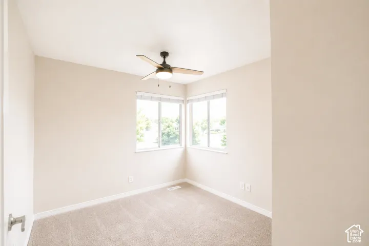 Neutral tone walls, carpeted flooring, corner windows with blinds, and ceiling fan with integrated lighting