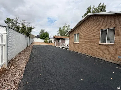 Brick exterior, asphalt paving, white vinyl fence, chain-link fence, and a separate structure with a ramp