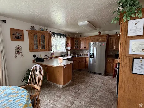 Kitchen featuring wood-finish cabinetry, stainless steel refrigerator, tile flooring, and a peninsula counter