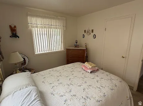 Comfortable bedroom with natural light from vertical blinds, wood-finish dresser, neutral wall coloring, and direct door access