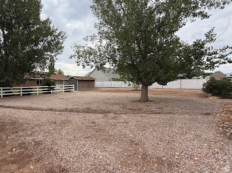 Spacious lot featuring mature trees, a white fence, and a gravel surface