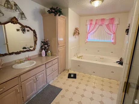 Vanity with integrated sink, built-in storage cabinetry, jetted soaking tub, and tile flooring