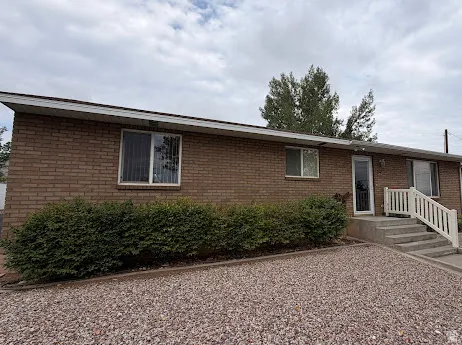 Brick exterior with multiple windows, concrete entry steps, white railing, and a gravel front area