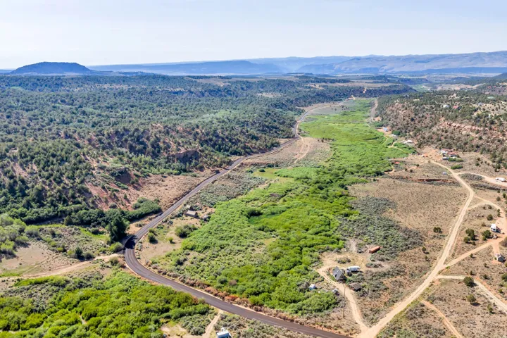 Expansive rural landscape featuring a winding paved road, diverse natural vegetation, and distant mountain ranges