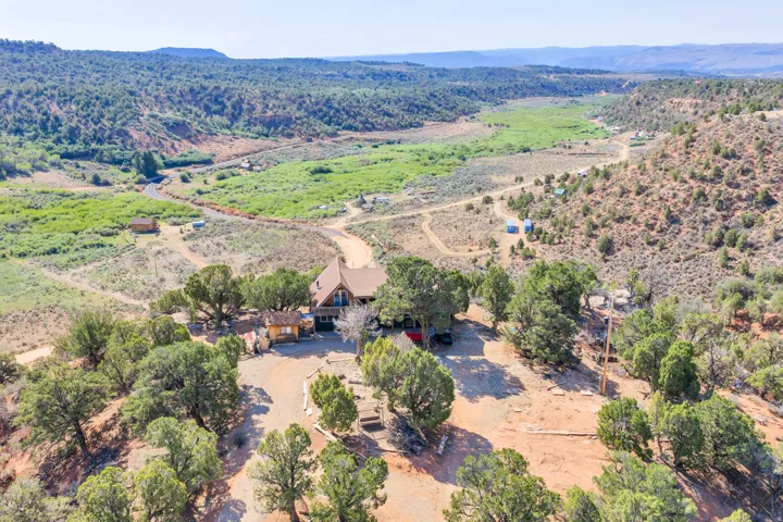 Elevated property with surrounding mature trees, a pitched roofline, and a gravel driveway, situated within a vast, verdant valley landscape