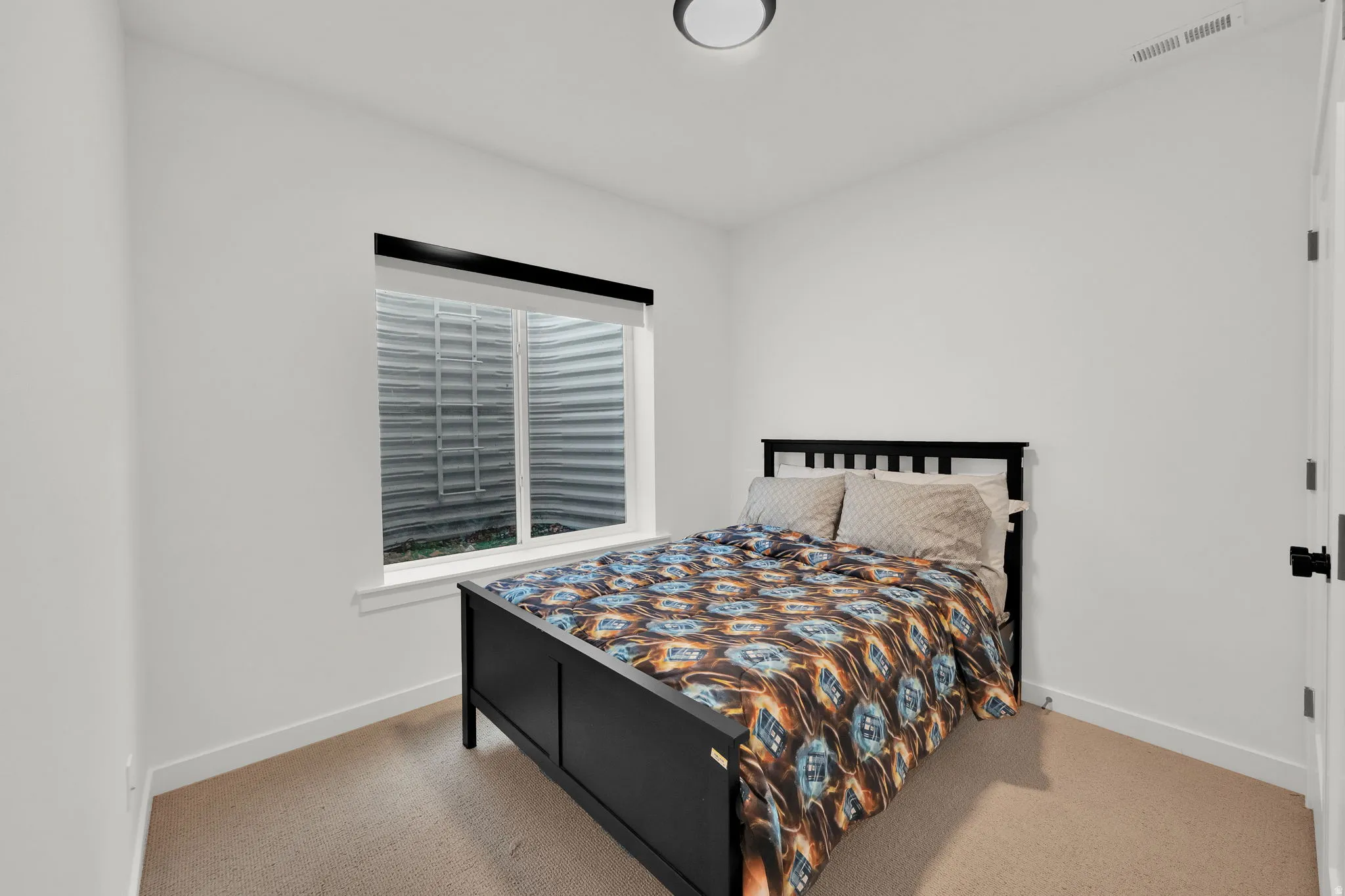Window with roller blind and exterior window well, light neutral wall paint, and ceiling-mounted flush light fixture