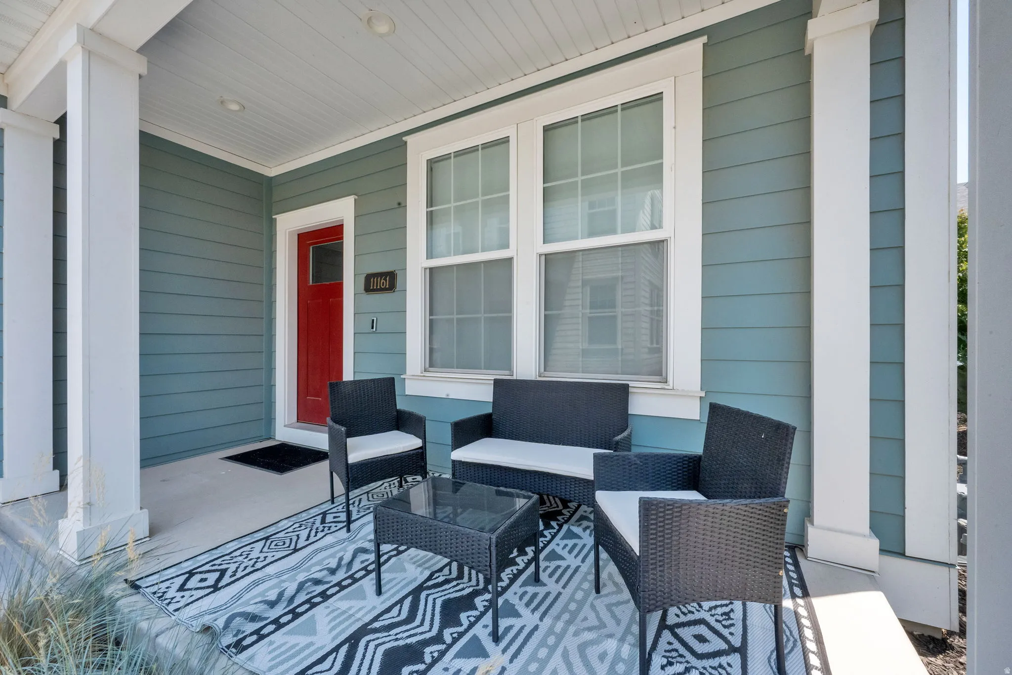 Covered front porch featuring a red entry door, horizontal siding, and multiple windows with white trim