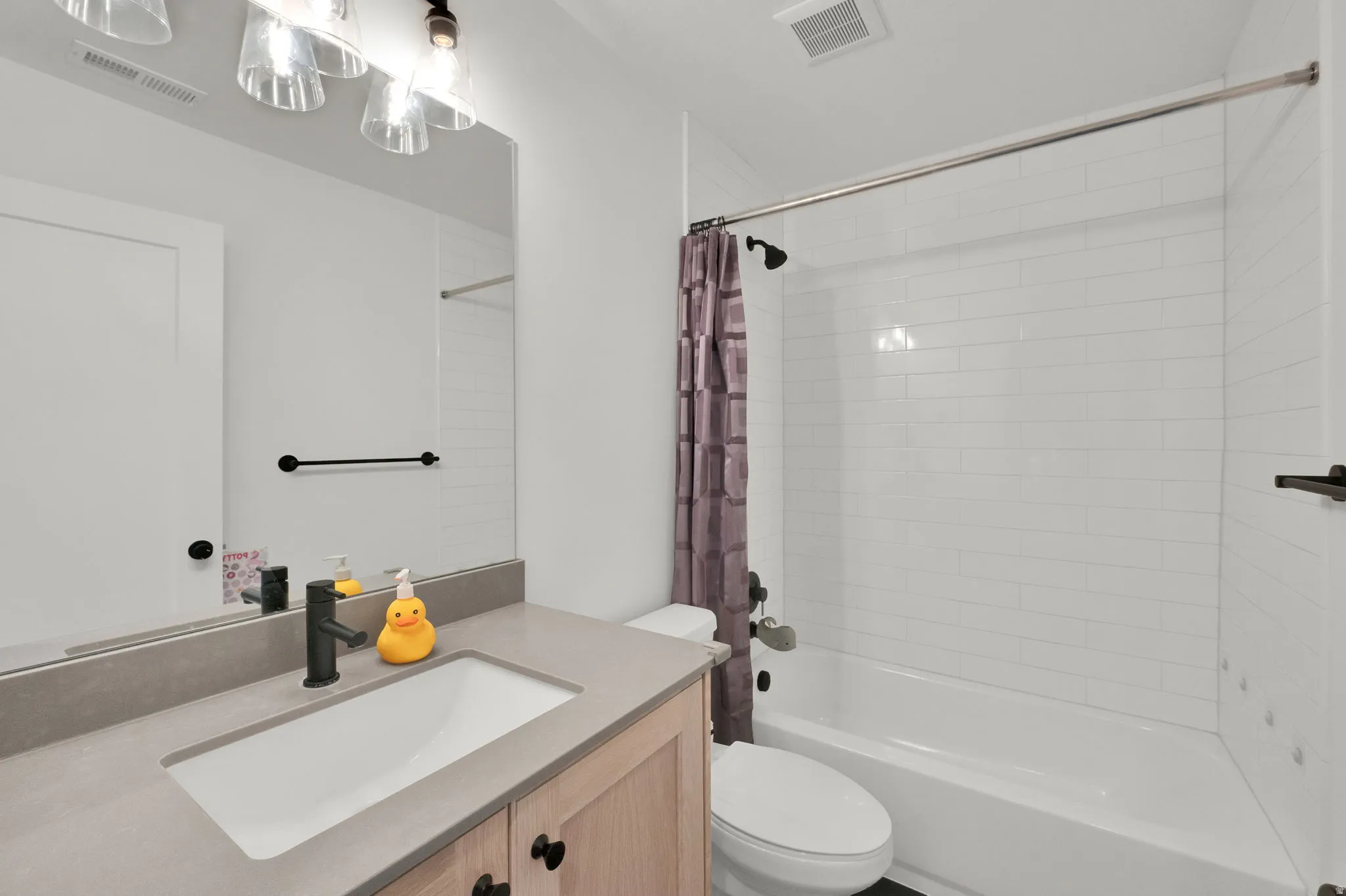 Light wood-finish vanity with a single basin sink, matte black faucet, and a stone-finish countertop