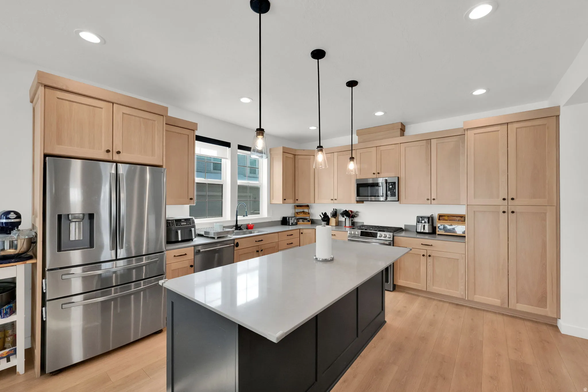 Light wood-finish cabinetry, stainless steel appliances, central island with light-toned countertop, and recessed lighting