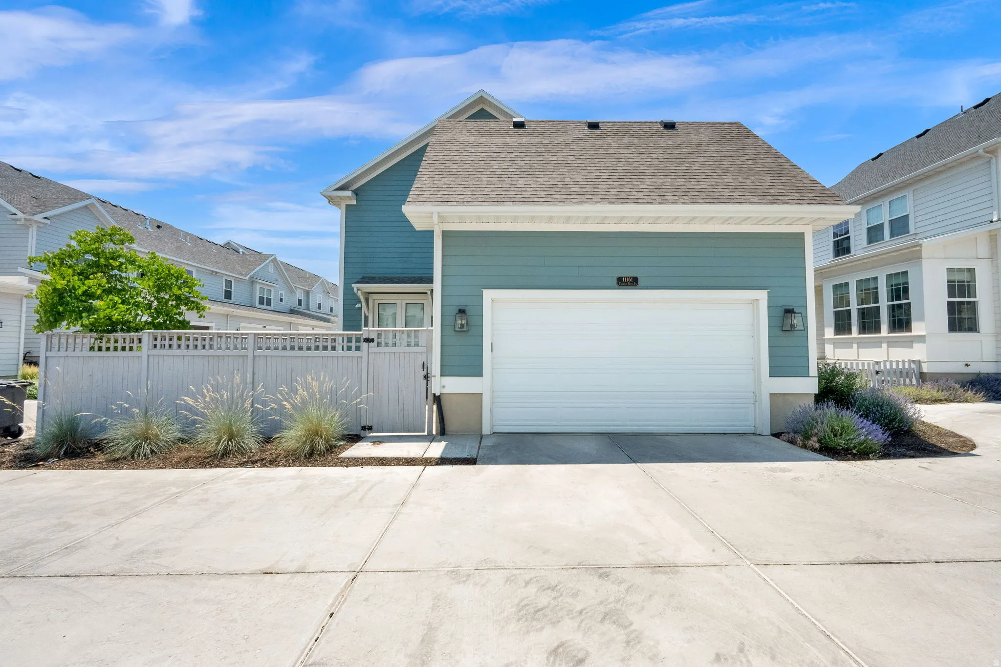 Attached two-car garage with a white door, exterior sconces, and siding in a blue-green finish
