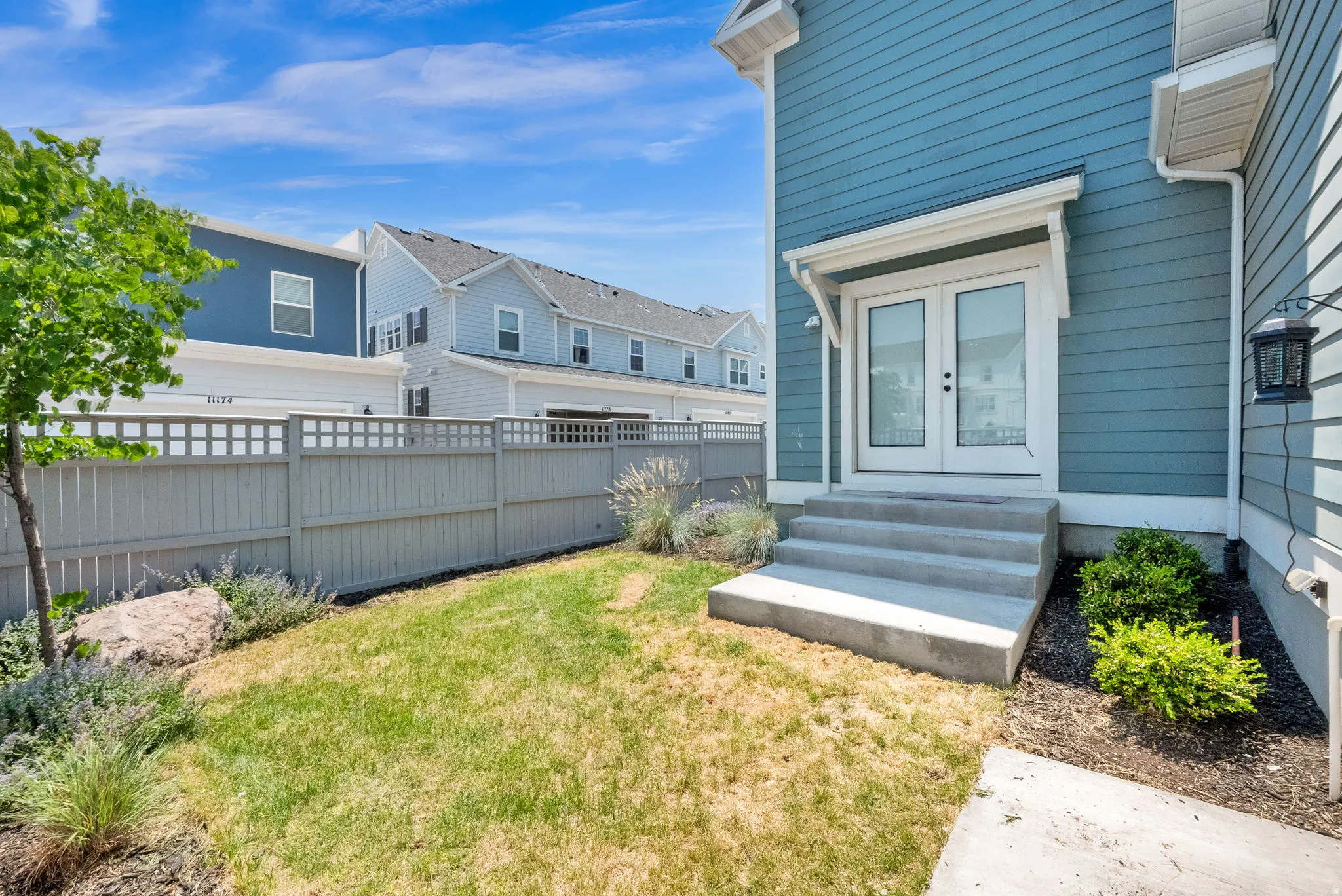 Exterior featuring horizontal siding, double glass doors with transom, concrete steps, and a lattice-top fence