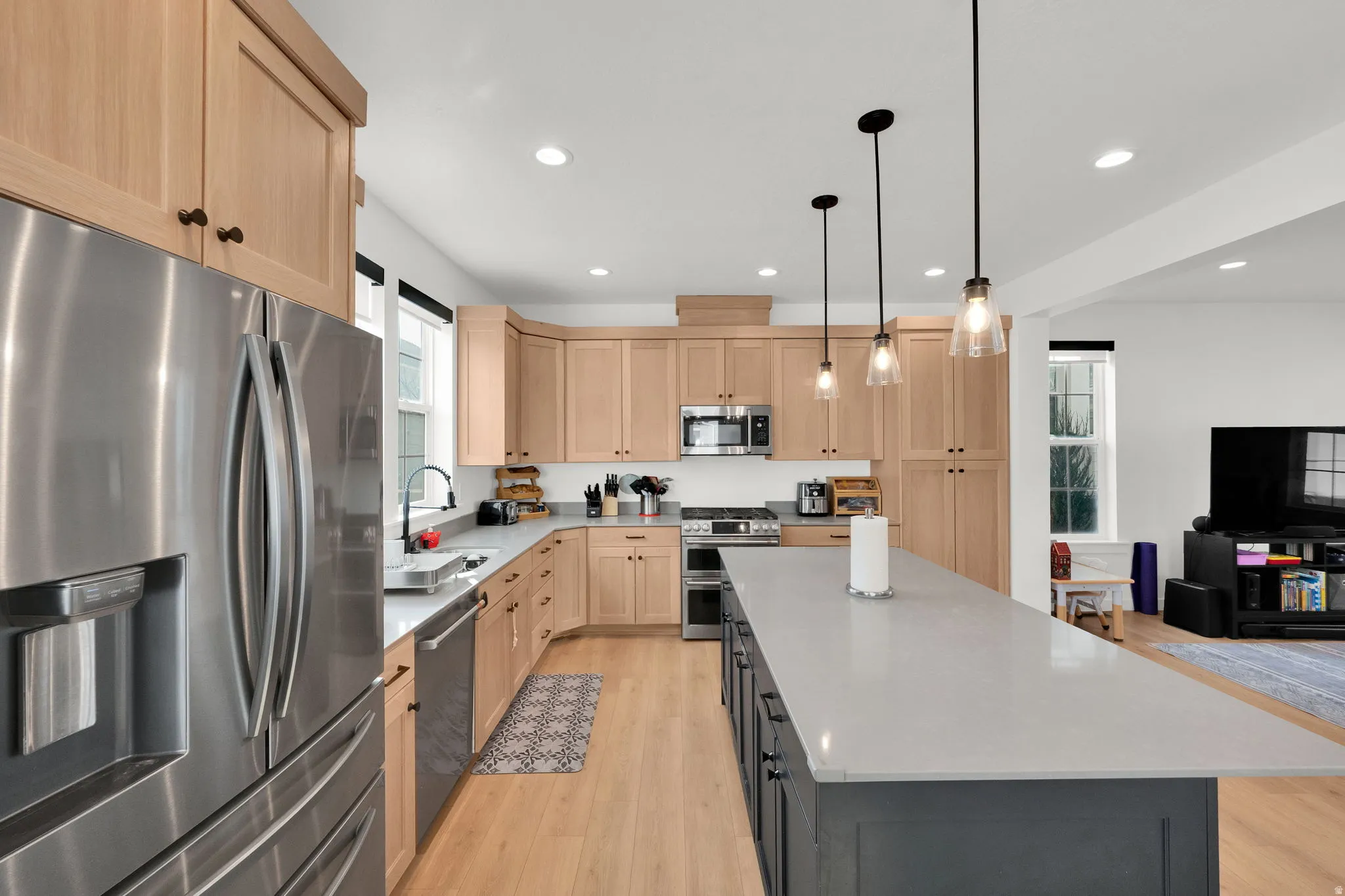 Stainless steel appliances, recessed lighting, wood-finish flooring, light wood cabinetry, and a large center island with pendant lighting