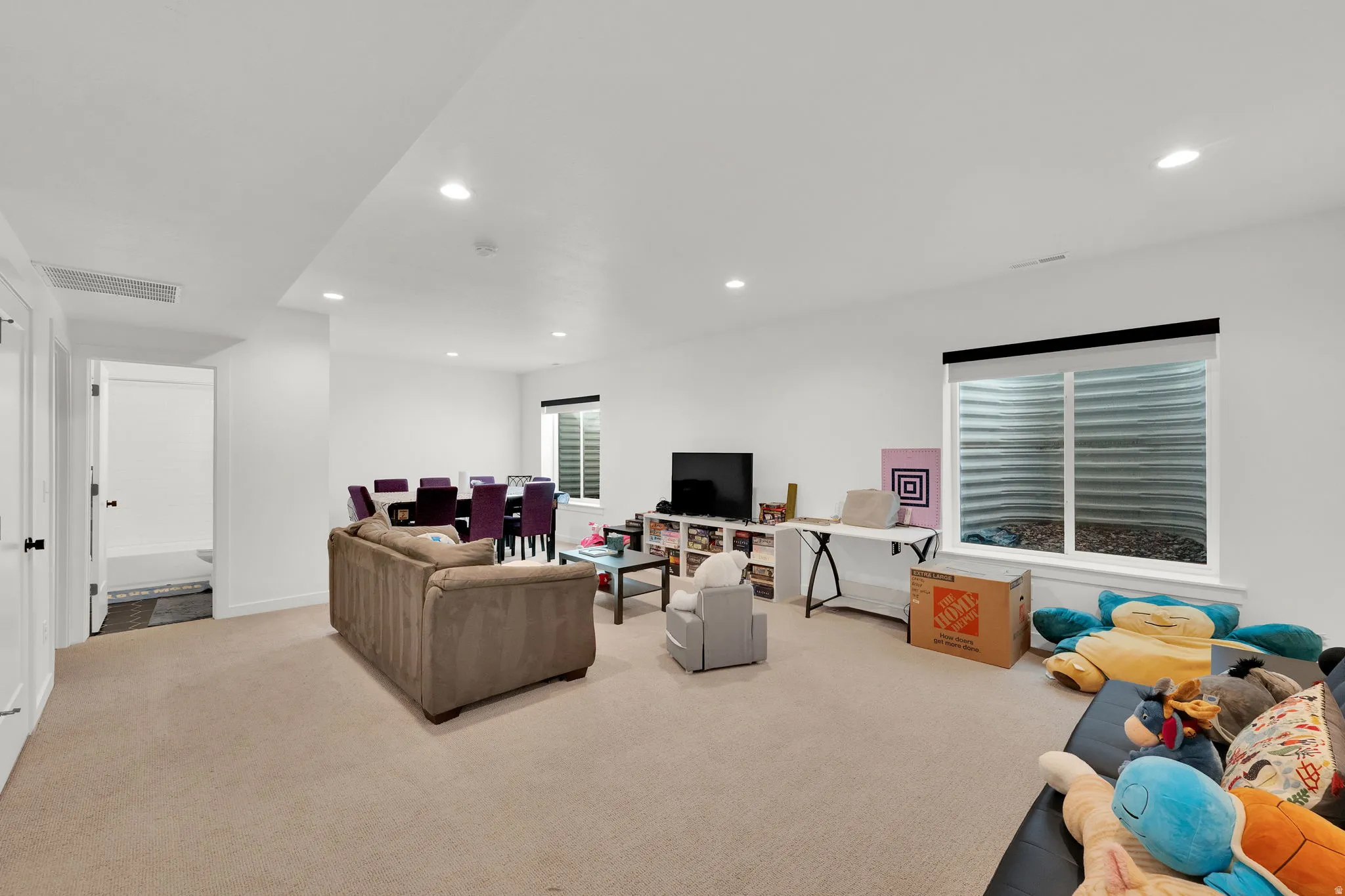 Recessed lighting illuminates the open-concept space featuring two windows, neutral carpeting, and white walls