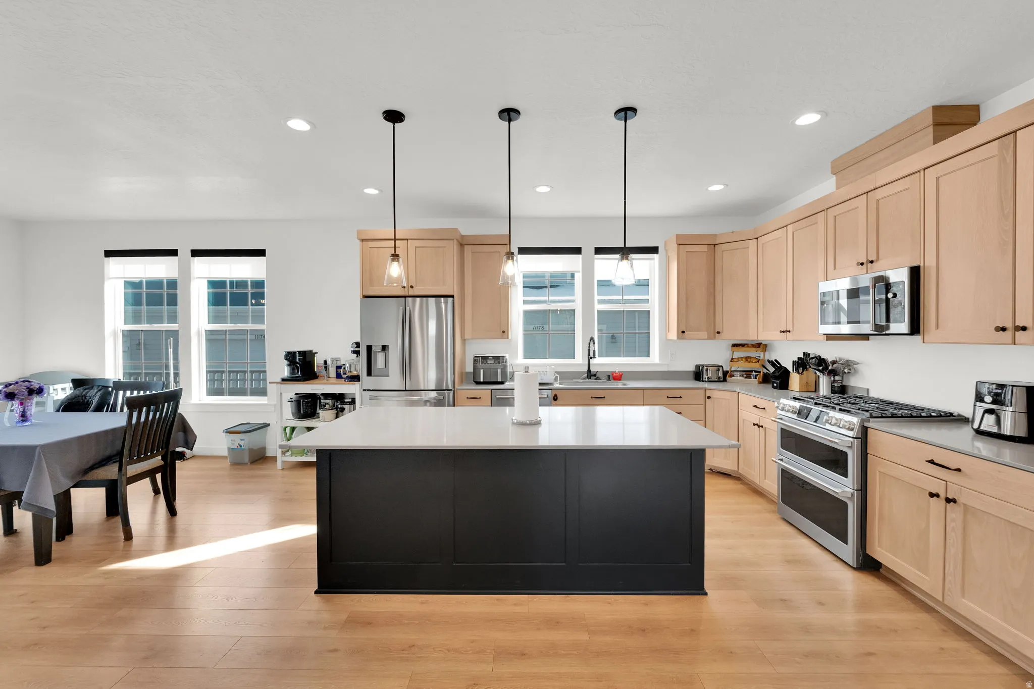 Open-concept kitchen featuring a dark island with a light countertop, light wood-finish cabinetry, stainless steel appliances, and wood-finish flooring